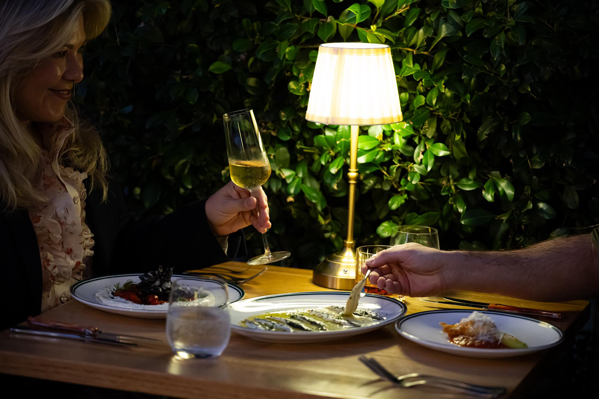 Diners raising a glass over sardines and shared plates under warm lamplight at Water St Kitchen